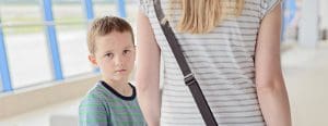 Little boy looking sadly at the camera holding moms hand in the airport