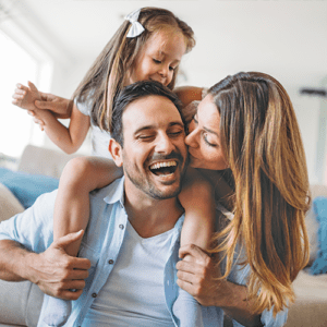 Mom kissing dad on the cheek while daughter sits on his shoulders